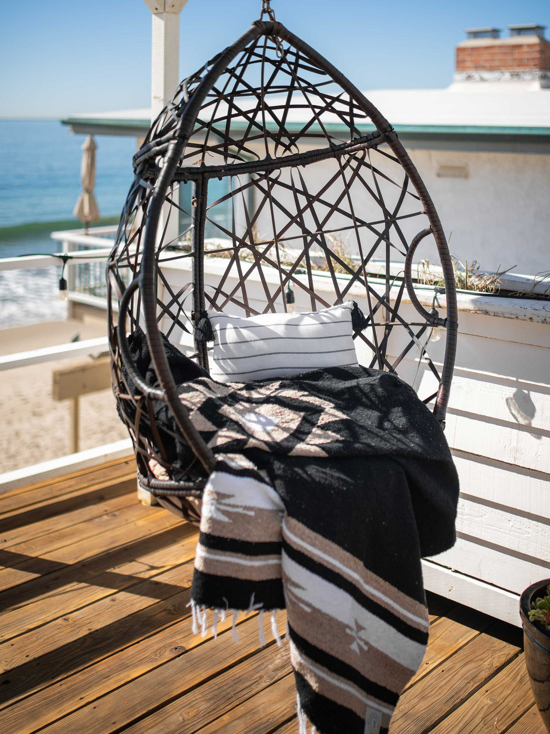 A black and Mexican blanket draped over a hanging char on a balcony overlooking the ocean.