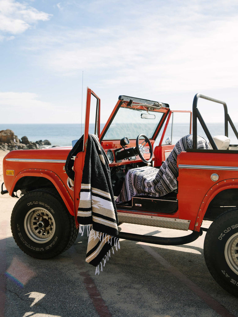 Black, white, and tan Mexican blanket draped over red bronco on California coast.