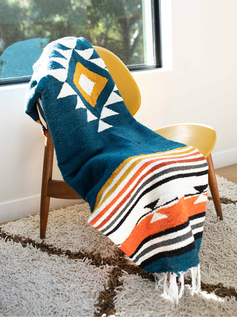 A navy blue, red, and yellow patterned Mexican throw blanket draped over an indoor chair.