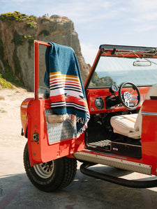 Large Navy Mexican blanket draped over red bronco jeep on the California Coast.
