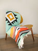 A green, red, and yellow patterned Mexican throw blanket draped over an indoor chair.