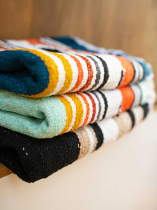 Close-up of three Mexican blankets in multi-colored, striped patterns folded on top of each other.