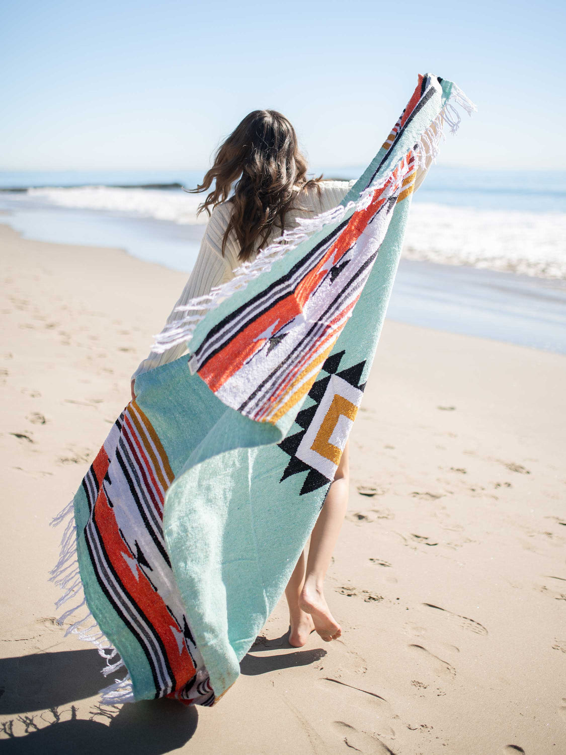 Woman on the beach wrapped in a teal and orange oversized Mexican blanket.