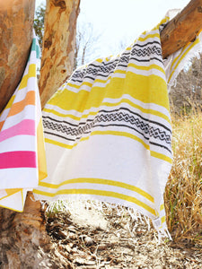A large, yellow and white patterned Mexican blanket draped over a tree branch blowing in the wind.