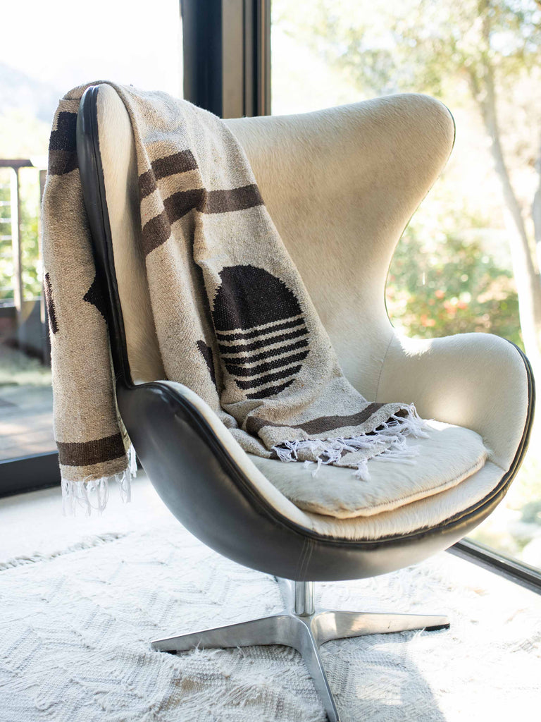 A tan and brown oversized Mexican blanket draped over the back of an indoor modern chair.