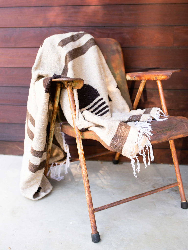 A large, brown Mexican blanket draped over an outdoor metal chair.