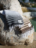 A gray and white striped Mexican blanket folded on top of a brown and tan striped Mexican blanket poolside.
