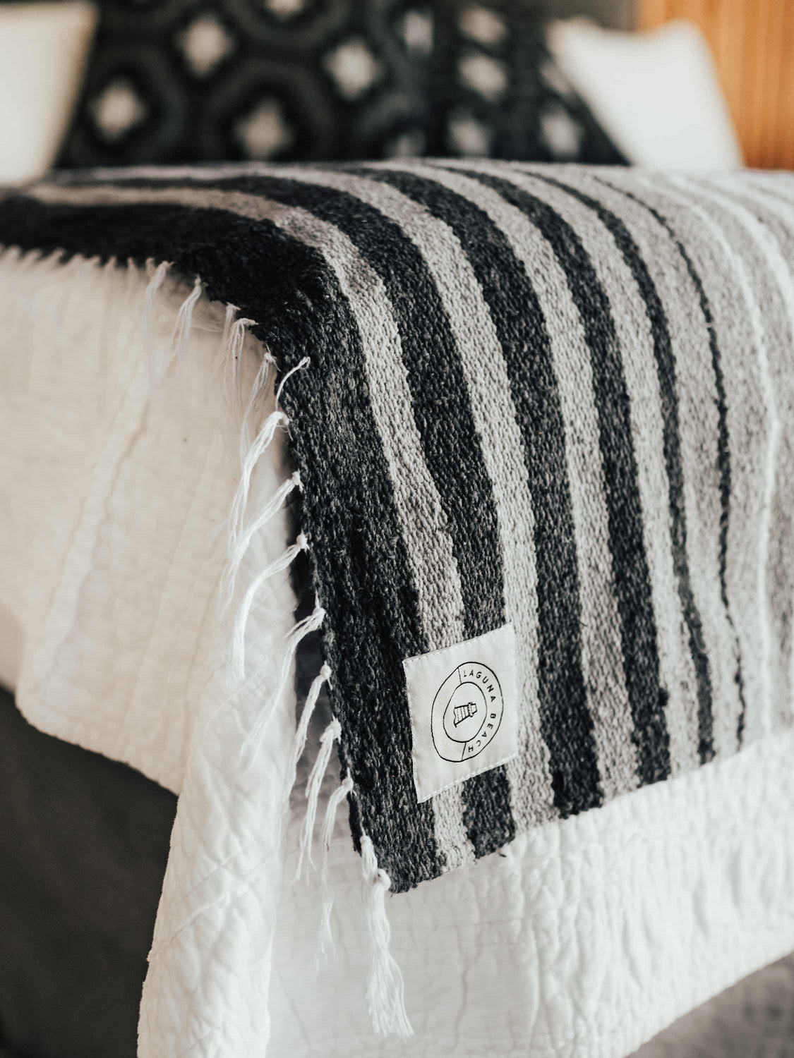 Close-up of a large, gray and white striped Mexican throw blanket decoratively draped over the foot of a bed.