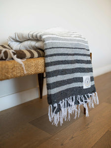 Large, gray and white striped Mexican blanket folded and draped over a wicker bench.