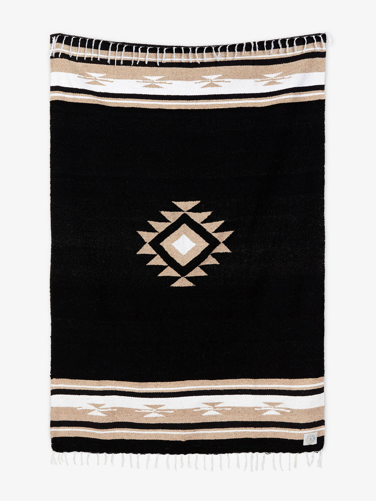  Oversized, traditional Mexican blanket in black, tan, and white pattern with white fringe spread out. 