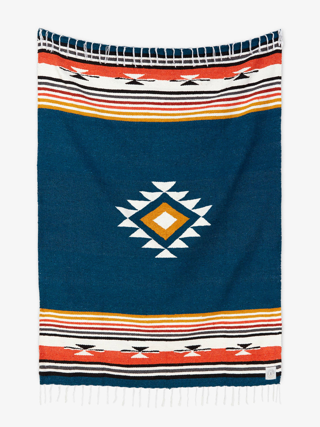 Oversized, traditional Mexican blanket in navy blue, red, and yellow pattern with white fringe spread out. 