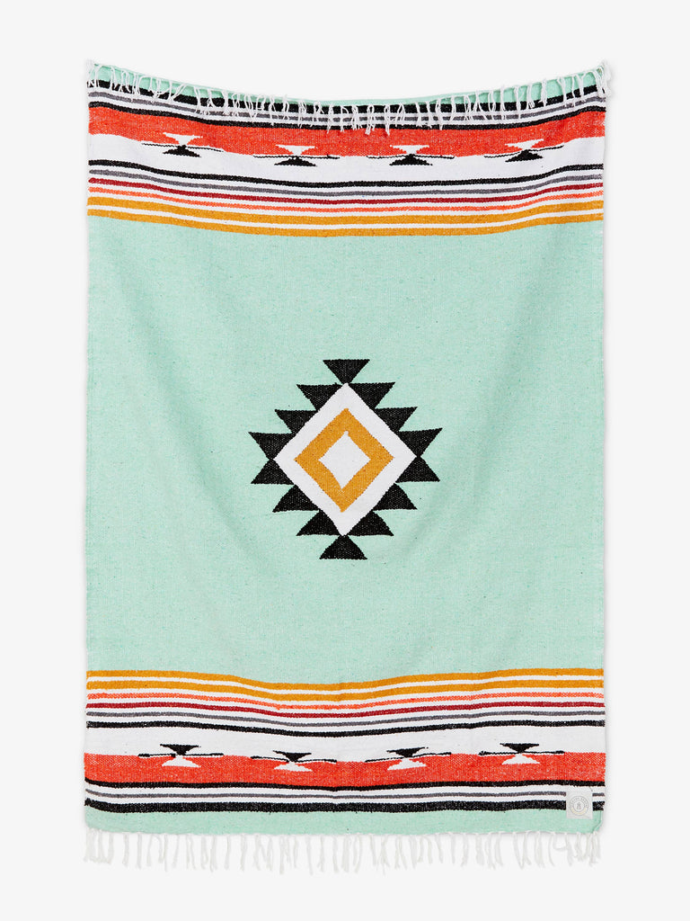Oversized, traditional Mexican blanket in green, red, and yellow pattern with white fringe spread out. 
