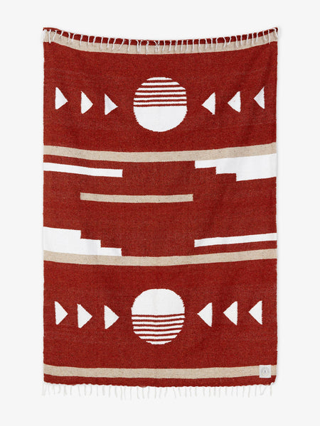 Oversized, hand-woven Mexican blanket in red with patterned designs and white fringe spread out.