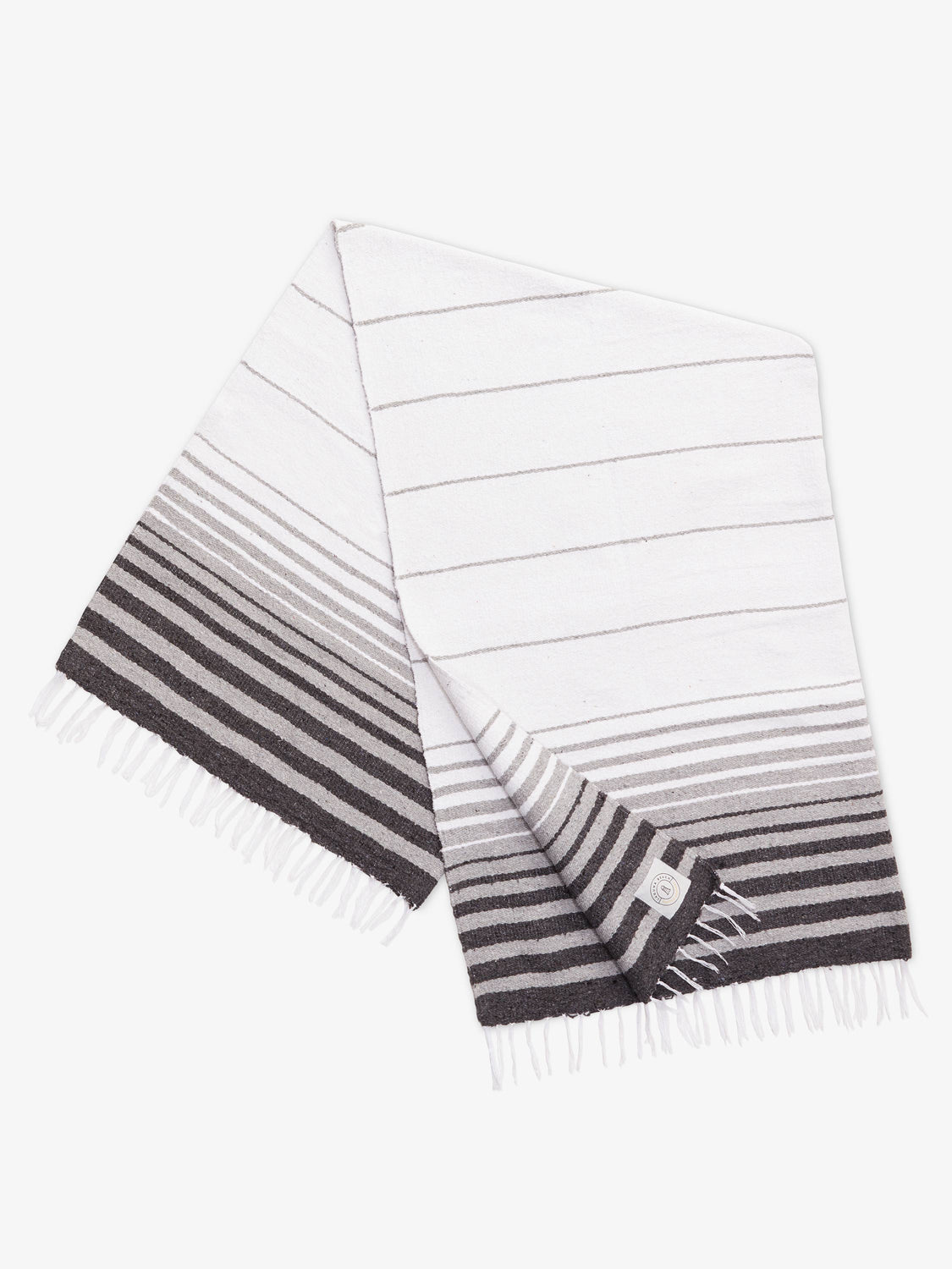 A folded traditional, hand-woven Mexican blanket in gray and white stripe pattern with fringe.