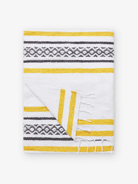 A folded traditional, hand-woven Mexican blanket in yellow and white pattern with fringe.