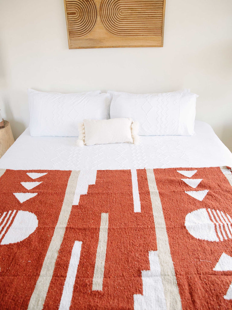 Red and tan Mexican blanket on bed in mordern white bedroom.