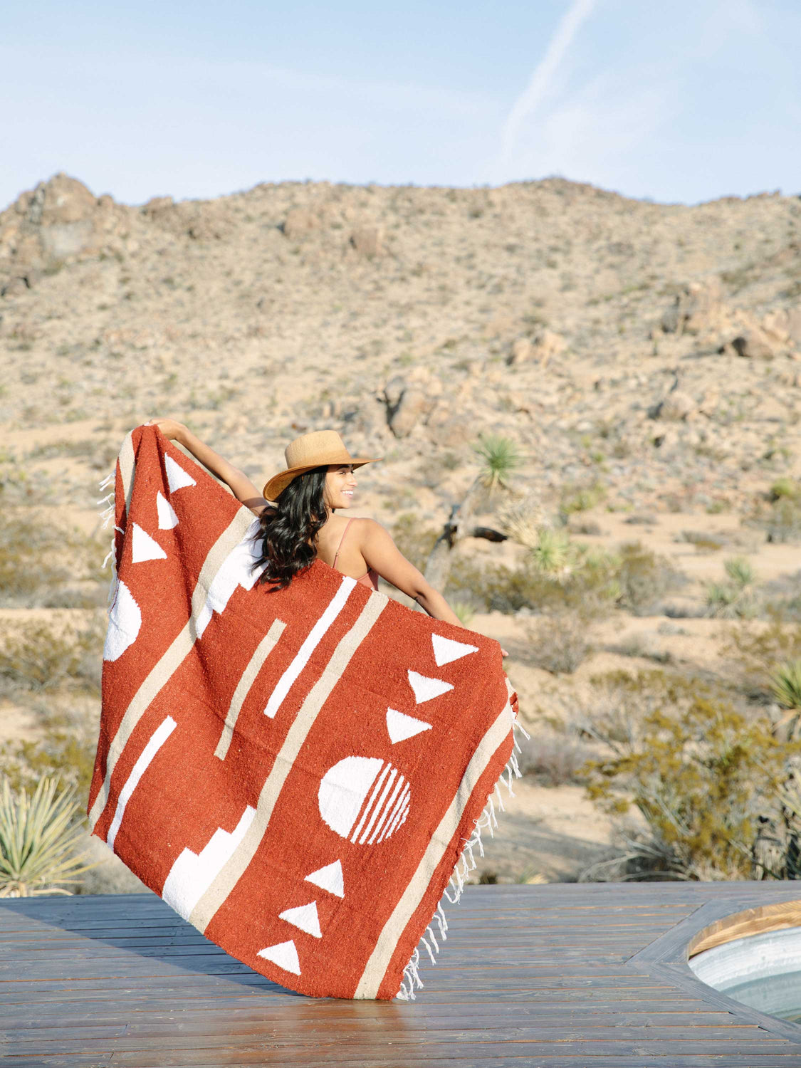 Woman in desert with red, tan, and white oversized Mexican blanket.
