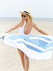 A woman looking back as she holds an oversized light blue and white striped microfiber beach towel spread out behind her.