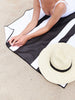 A close-up of a woman laying out at the beach on an extra large, quick drying black and white striped microfiber beach towel.