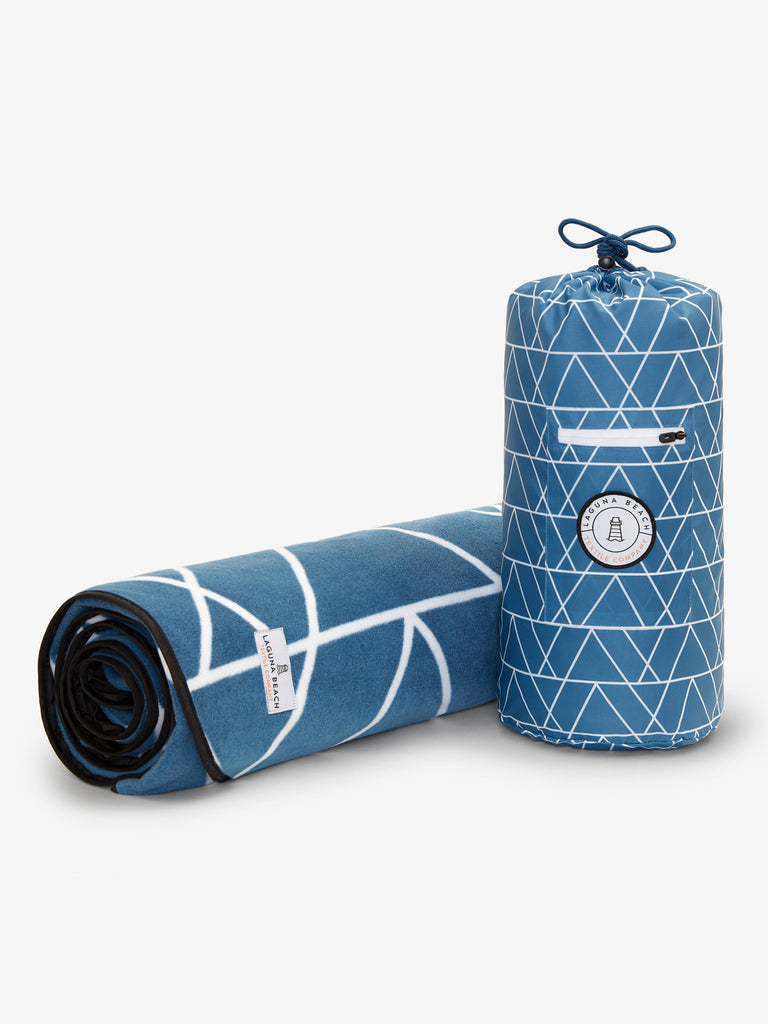 A rolled up, blue and white mountain patterned waterproof picnic and outdoor blanket next to a matching compact travel case.