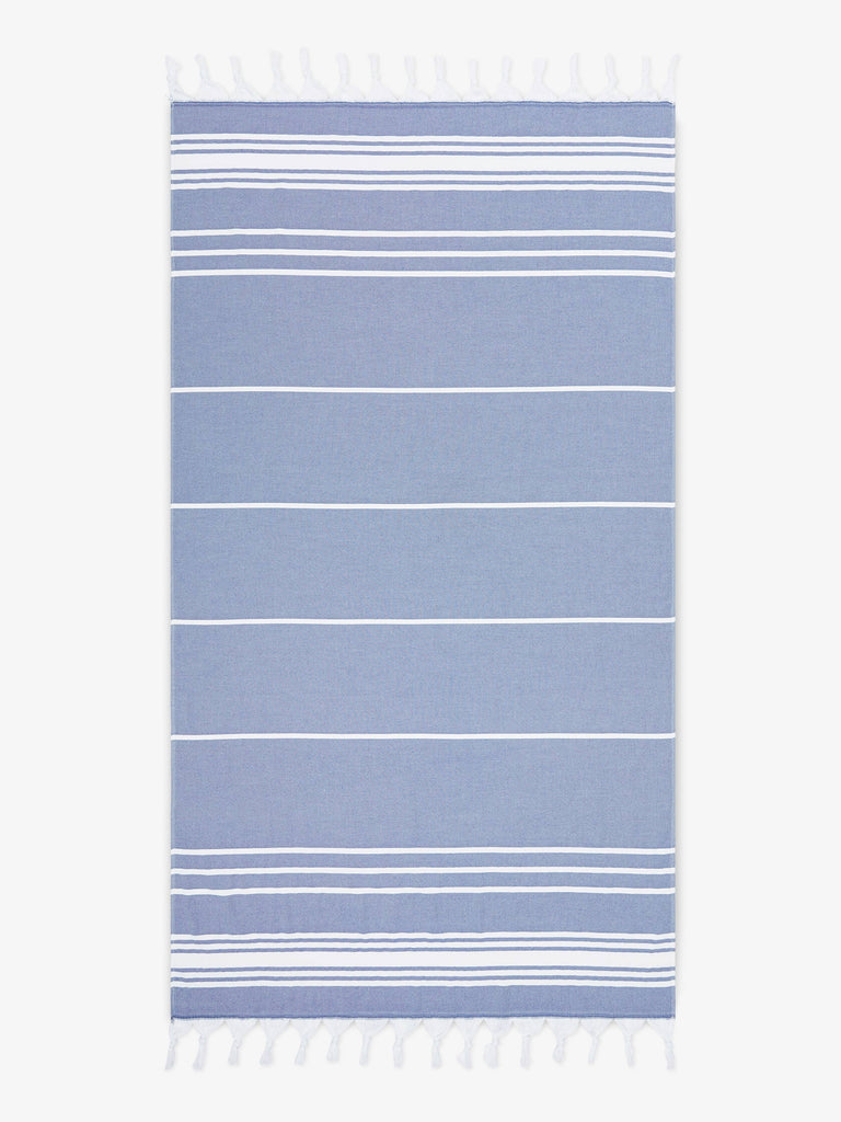 An oversized, blue and white striped Turkish cotton towel with white fringe laid out.