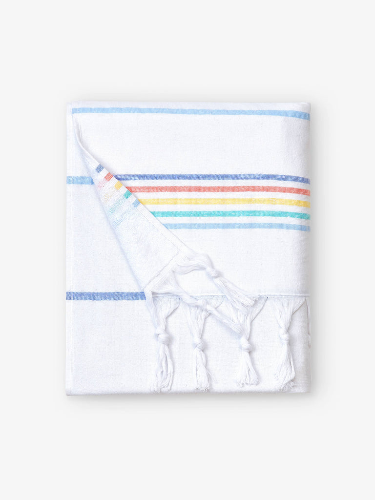A folded white and rainbow striped Turkish towel with white fringe.