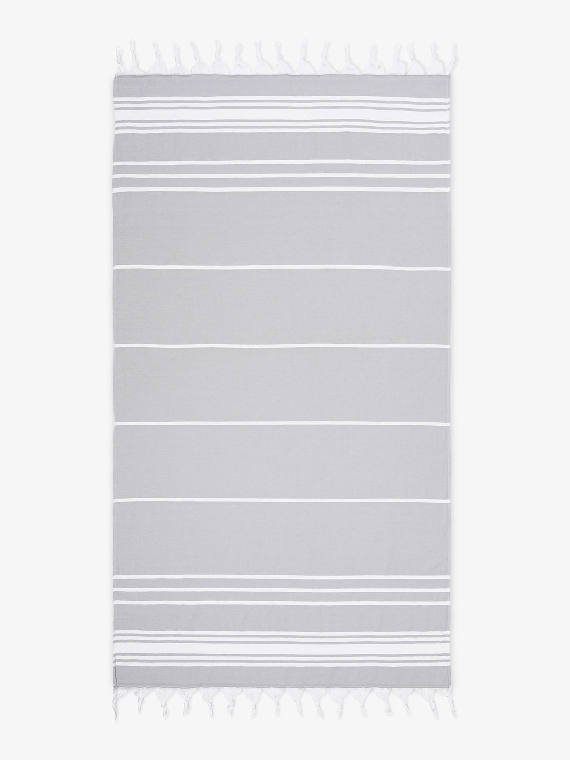 An oversized, gray and white striped Turkish cotton towel with white fringe laid out.