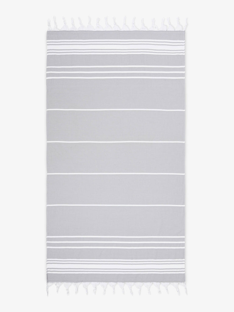 An oversized, gray and white striped Turkish cotton towel with white fringe laid out.