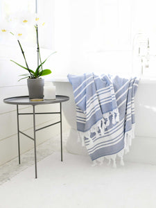 An extra large, blue and white striped Turkish bath towel hanging over a bathtub.