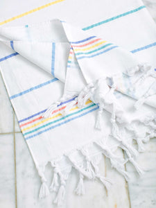 A folded white and rainbow striped Turkish bath towel laid out on the bathroom floor.
