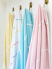 Four extra large striped Turkish towels—yellow, multicolor, aqua blue, and pink—hanging side by side.
