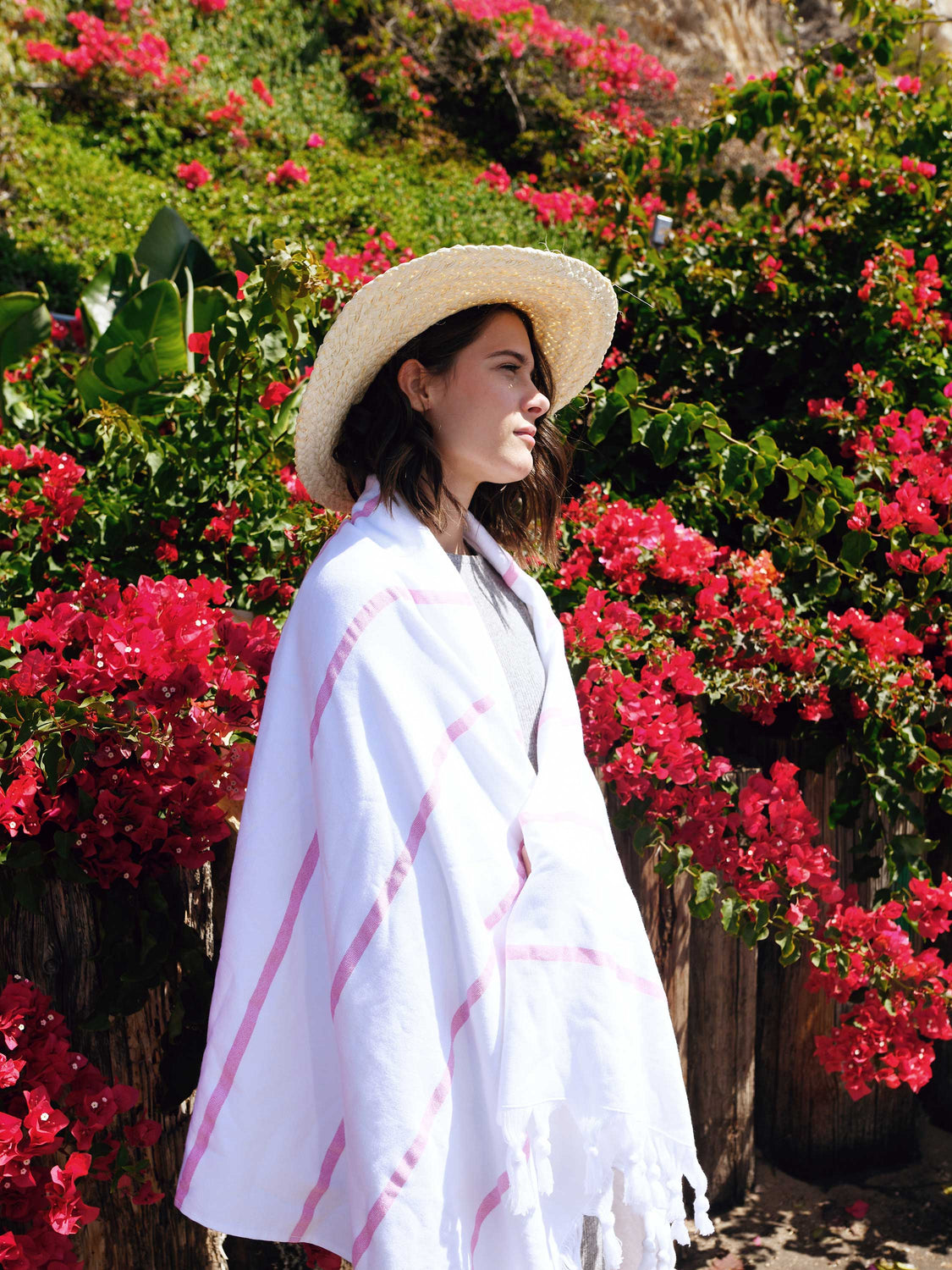 A woman standing in front of a hill of flowers, wrapped in an oversized, white and pink striped Turkish towel.