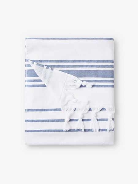 A folded white and blue striped Turkish towel with white fringe.