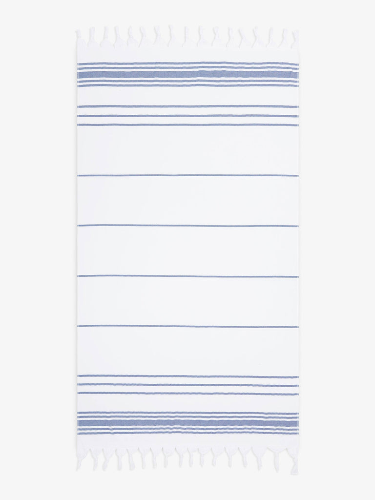 An oversized, white and blue striped Turkish cotton towel with white fringe laid out.