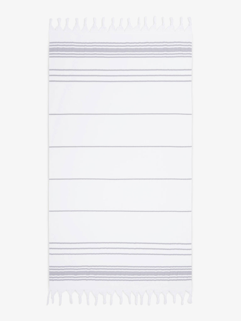 An oversized, white and gray striped Turkish cotton towel with white fringe laid out.