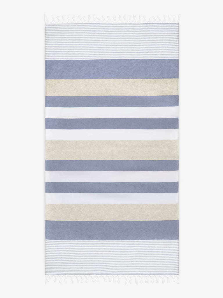An oversized, blue, white, and tan striped Turkish cotton towel with white fringe laid out. 