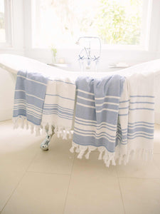 Four blue and white striped hand and beach Turkish towels draped over a porcelain bathtub.