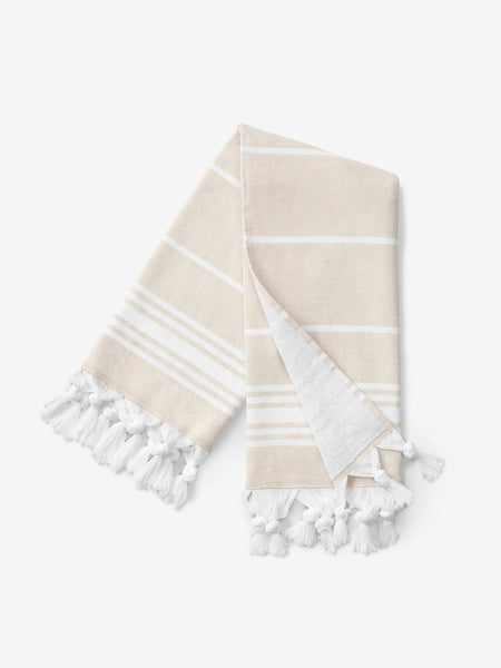A folded tan and white striped Turkish hand towel with white fringe.