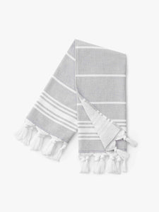 A folded stone and white striped Turkish hand towel with white fringe.