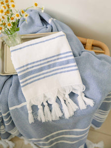 A folded blue and white striped Turkish hand towel with white fringe laying on a tray with flowers.