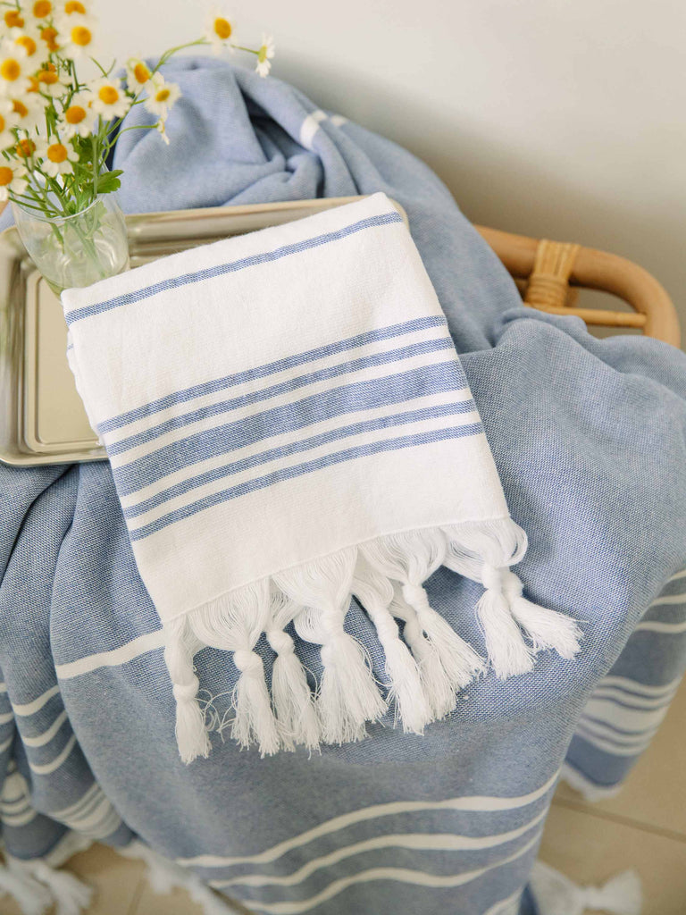A folded blue and white striped Turkish hand towel with white fringe laying on a tray with flowers.