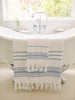 Two folded white and blue Turkish towels draped over a porcelain bathtub.