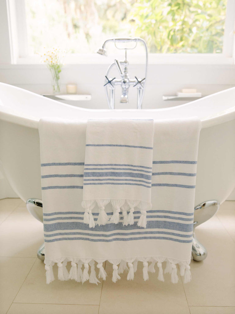 Two folded white and blue Turkish towels draped over a porcelain bathtub.