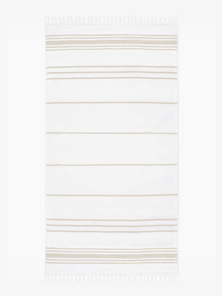 An oversized tan and white striped Turkish cotton towel with white fringe laid out. 