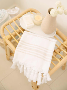 A folded tan and white striped Turkish hand towel with white fringe next to a small tray with flowers and a candle.
