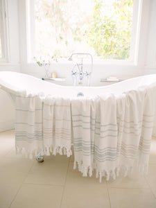 Four tan and white and gray and white striped hand and beach Turkish towels draped over a porcelain bathtub.