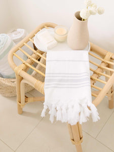 A folded gray and white striped Turkish hand towel with white fringe laying on a tray with a candle and flowers.