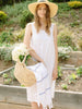 A woman standing in the garden holding a basket with flowers and a navy and white striped Turkish towel.