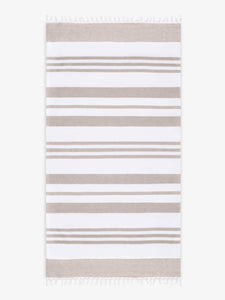 An oversized, tan and white striped Turkish cotton towel with white fringe laid out. 