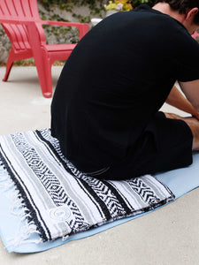 A man sitting on top of a folded Mexican blanket and powder blue yoga mat towel.